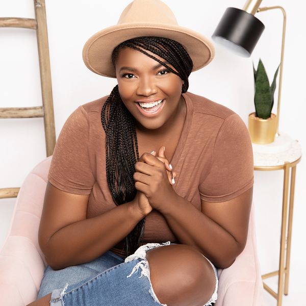 African American woman smiling with a brown shirt and denim ripped jeans.