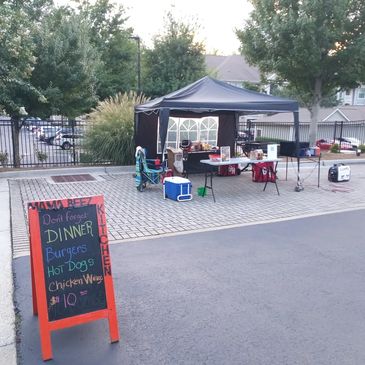 Outdoor food stand with a menu board listing dinner items like burgers and hot dogs.