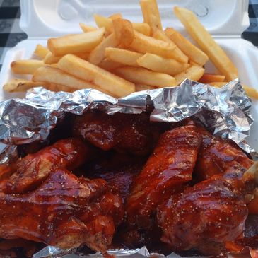 Barbecue chicken wings with crispy French fries in a takeout container.