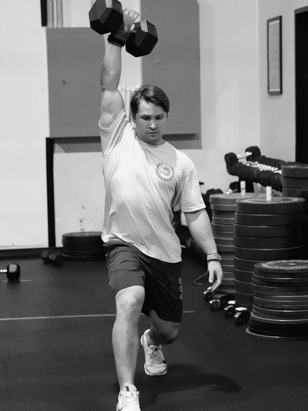 Man doing dumbbell overhead lunge at gym.