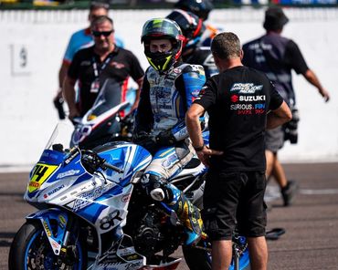 Motorcycle racer sitting on a blue and white Suzuki bike.