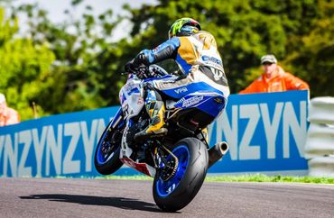 Motorcyclist performing a wheelie on a racetrack.