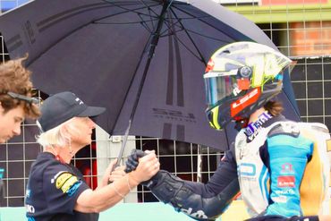 Two people shaking hands under a large umbrella.