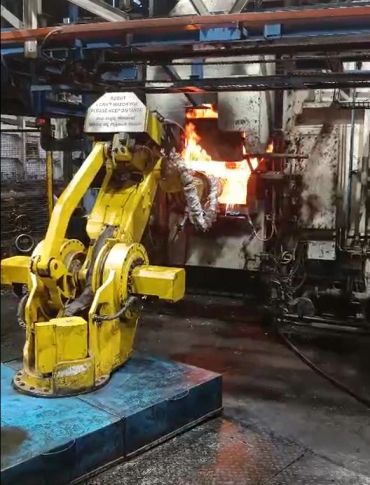 Industrial robot arm working with molten metal in a factory.