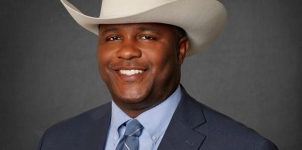 Man in a suit wearing a cowboy hat, smiling.