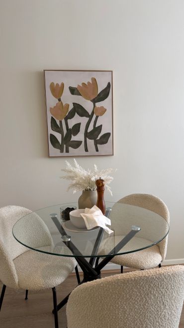 Minimalist dining area with glass table and floral artwork.