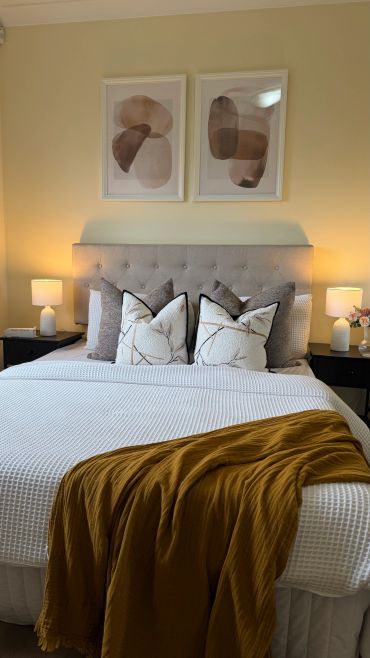 Cozy bed setup with neutral pillows, mustard throw, and abstract wall art.