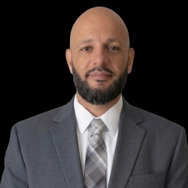 Professional man in a gray suit with a patterned tie against a black background.