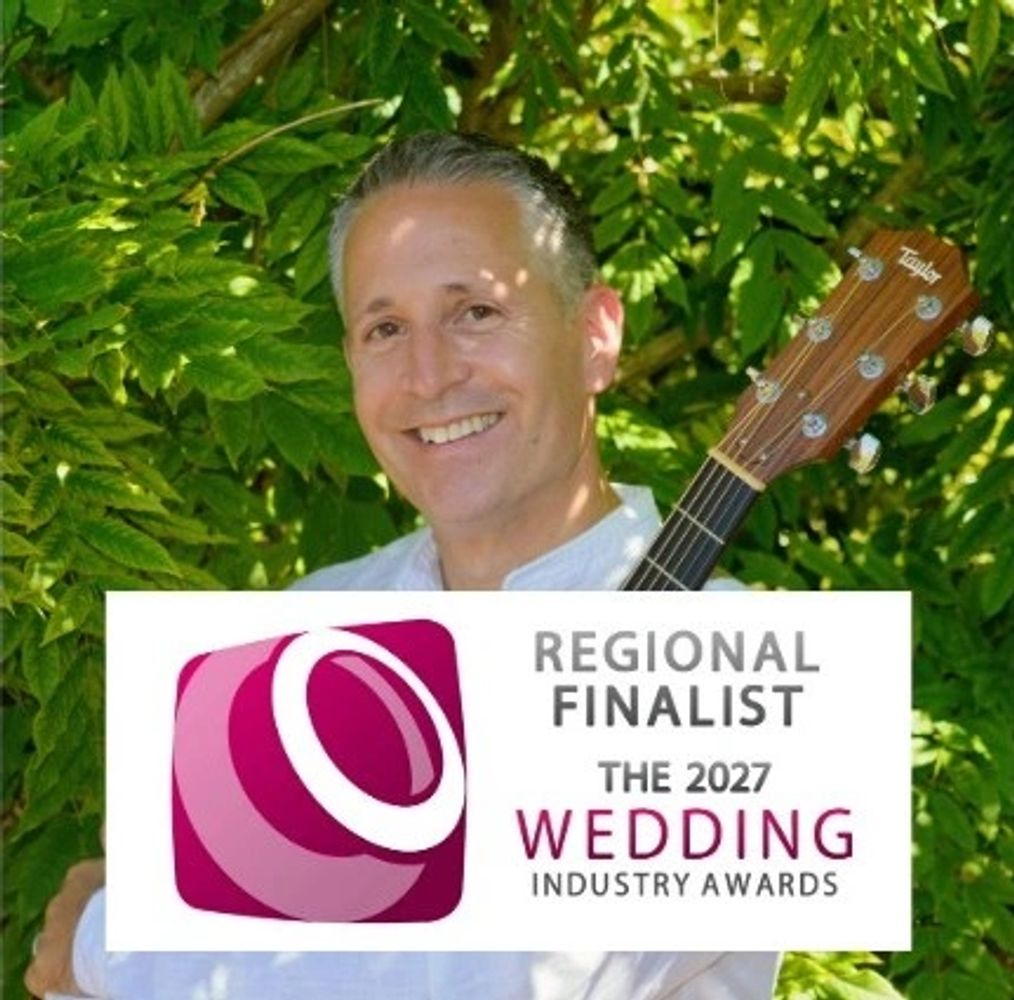 Smiling Tom with guitar and wedding awards finalist sign.