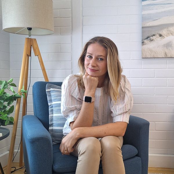 A woman sits thoughtfully in a cozy, well-decorated room with plants and soft lighting.