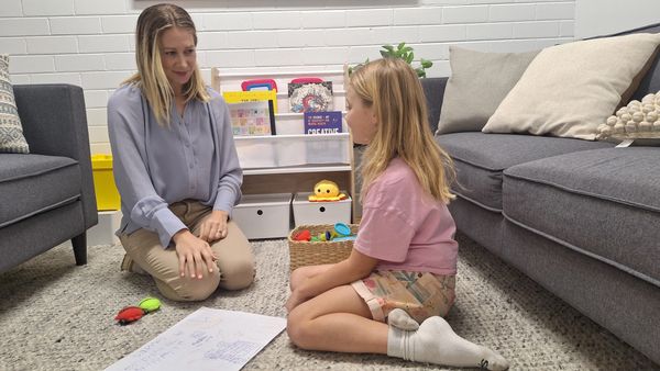 Woman and girl sitting on carpet, engaging in a calm conversation.