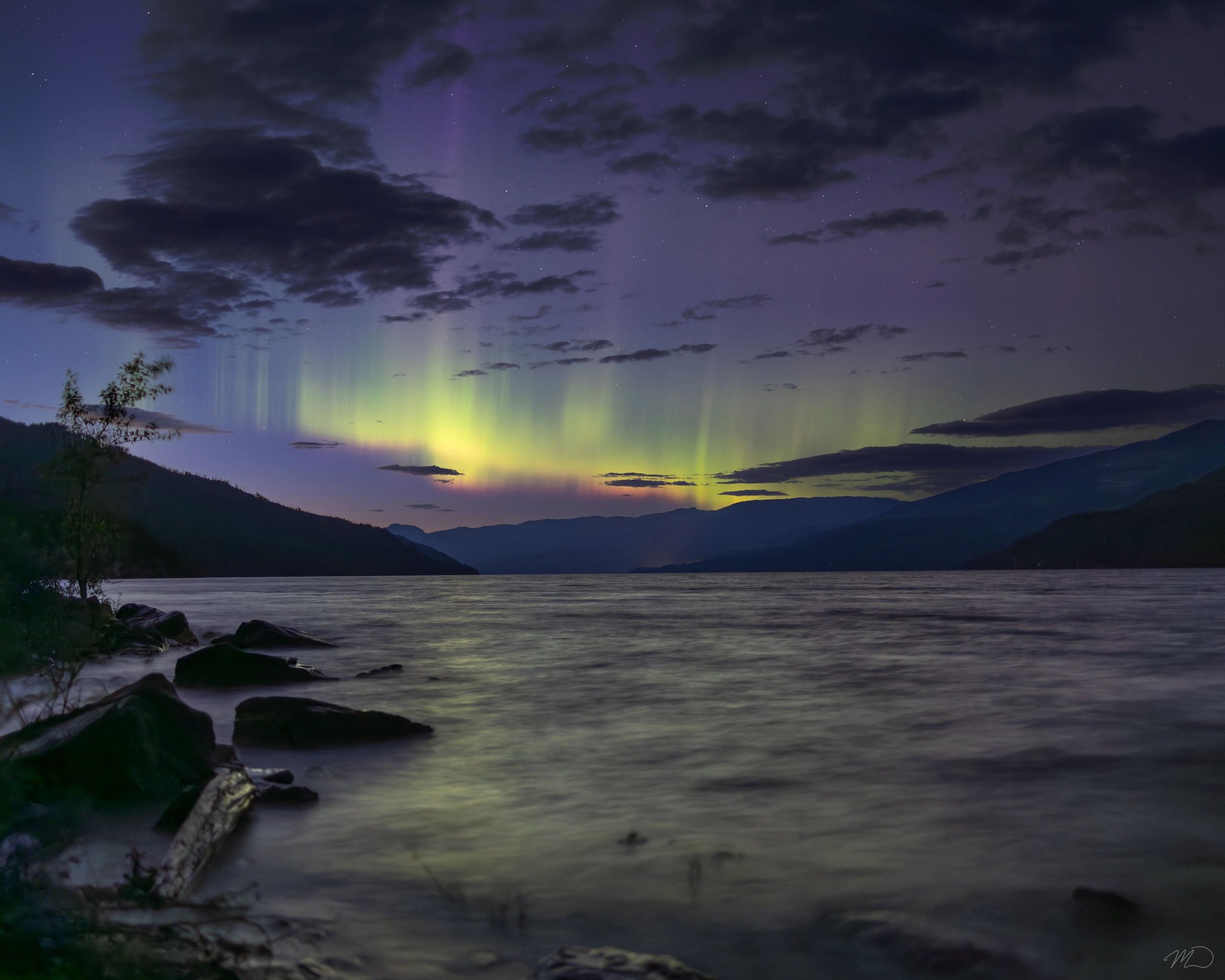 Northern lights in a twilight sky over a mountain lake.