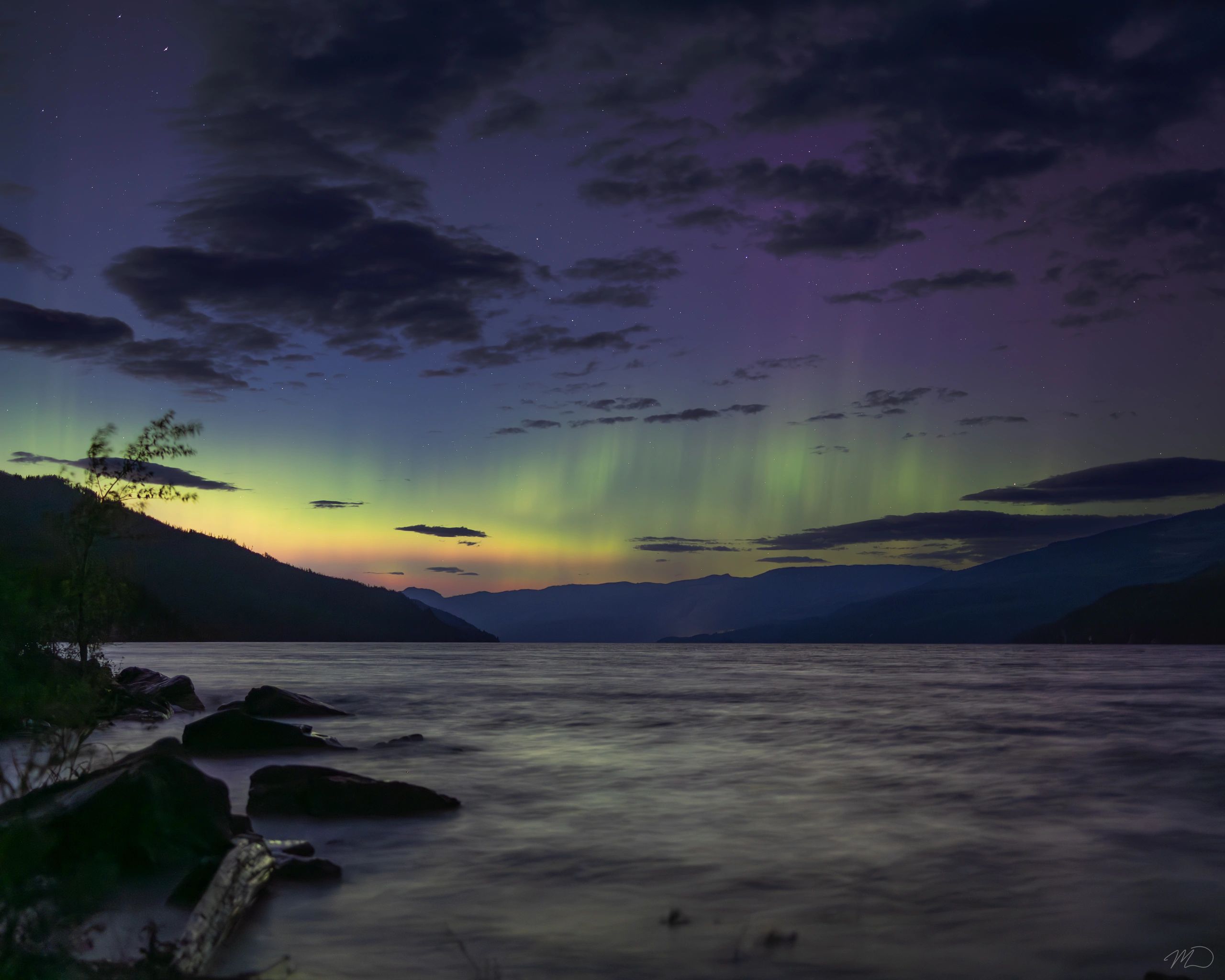 Night sky with northern lights over a lake and mountains.