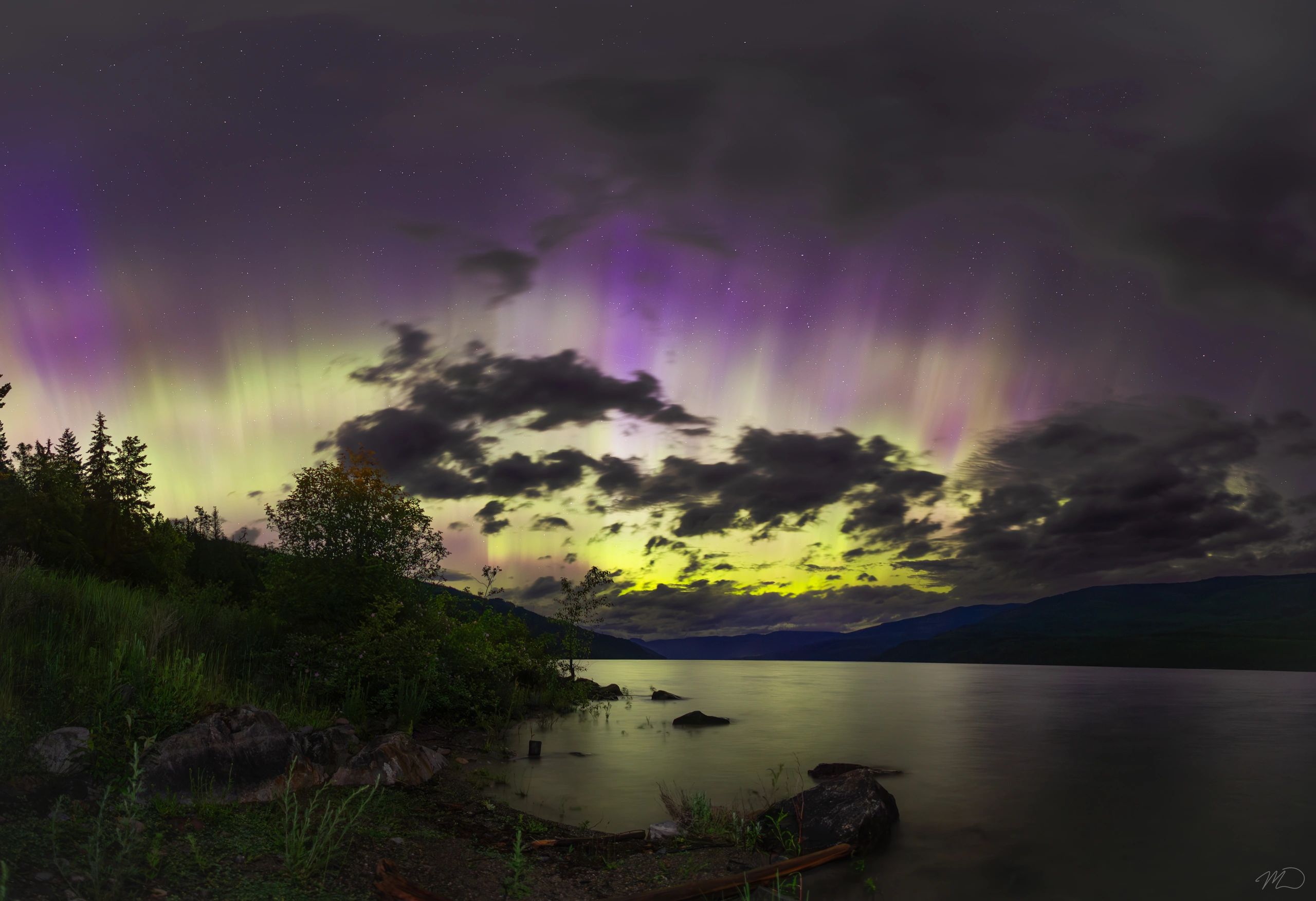 Northern lights over a lake with trees and clouds at night.