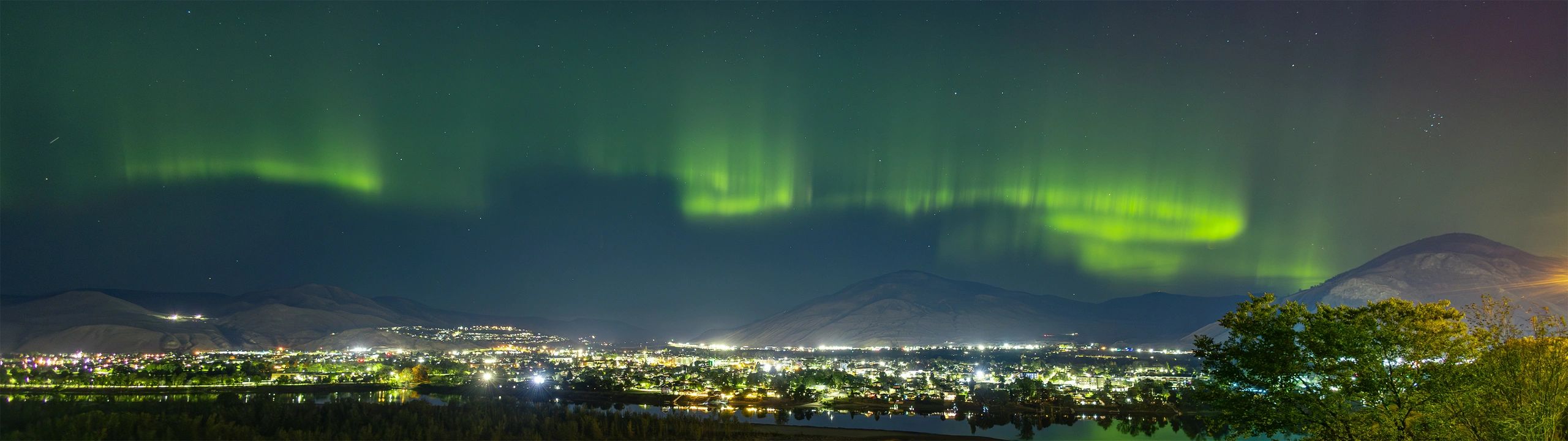 Northern lights over a city at night with mountains in the background.