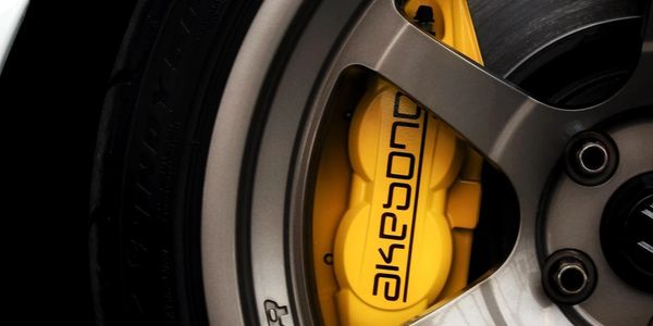 Close-up of a yellow Akebono brake caliper behind a car wheel.