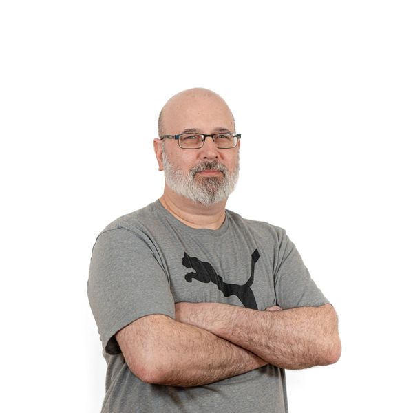 Confident middle-aged man with glasses and a beard in a grey Puma t-shirt.