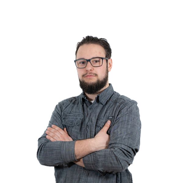 Man with glasses and beard crossing arms, wearing a gray shirt.