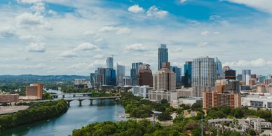 Skyline of a modern city with a river and bridges under a blue sky.