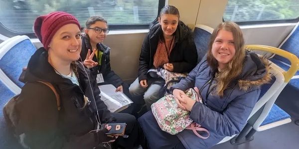A small group of people smiling while sitting on a public bus or train.
