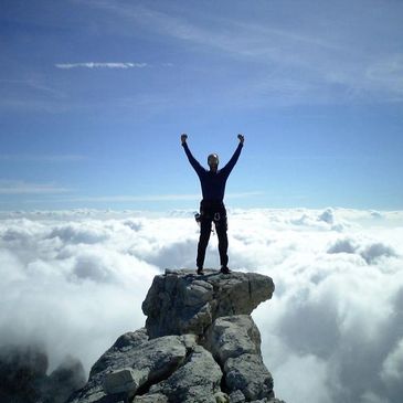 Person has scaled the mountain and is holding arms up to celebrate victory