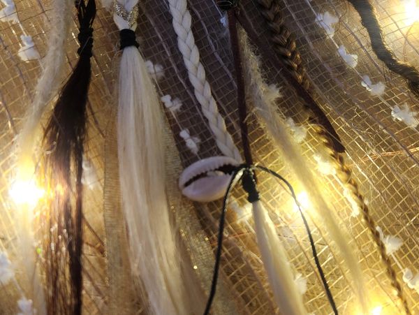 Braided hair strands and a shell hanging with warm lights in the background.