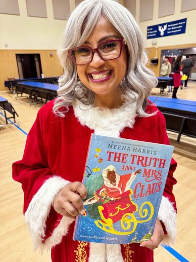 Woman in festive attire holding a children's book about Mrs. Claus.