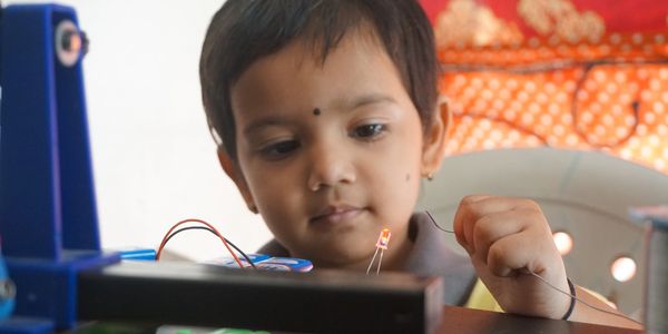 A young child focused on lighting an LED with wires and a battery.