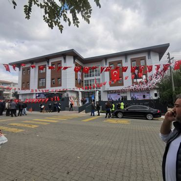 A building decorated with Turkish flags and people gathered outside under a cloudy sky.