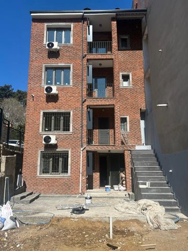 Three-story brick building under construction with external staircase and air conditioning units.