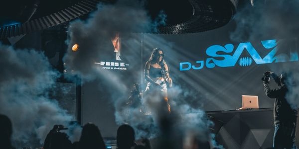 DJ Sav performing on stage with dramatic smoke effects and lighting.