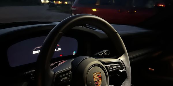 Interior view of a Porsche steering wheel at dusk with a red minivan outside.