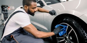 Man cleaning a car tire with a blue cloth in a garage.