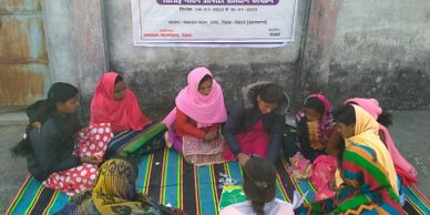 A group of women and girls sitting on a mat, engaged in discussion or study.