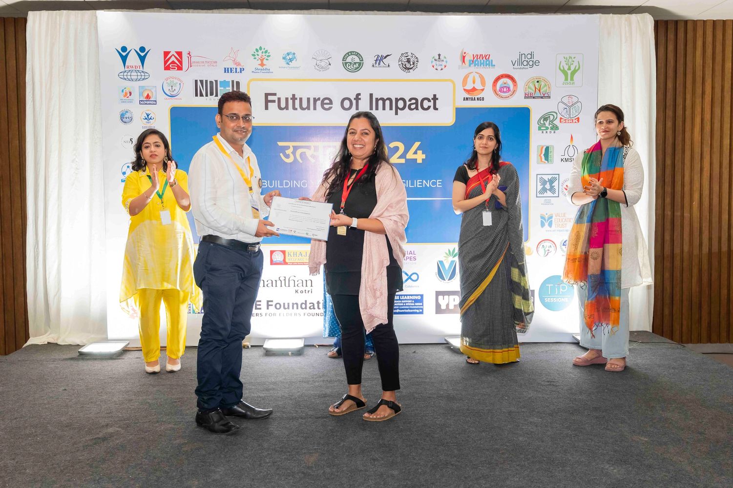 Certificate presentation ceremony at Future of Impact event with five people on stage applauding.