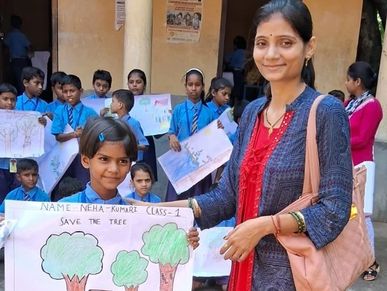 A girl holding a drawing about saving trees with a woman beside her and children in the background.