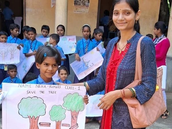 A young girl and woman hold a tree conservation poster among school children.