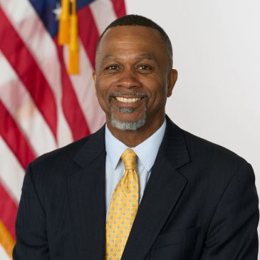 Smiling man in suit with an American flag background.