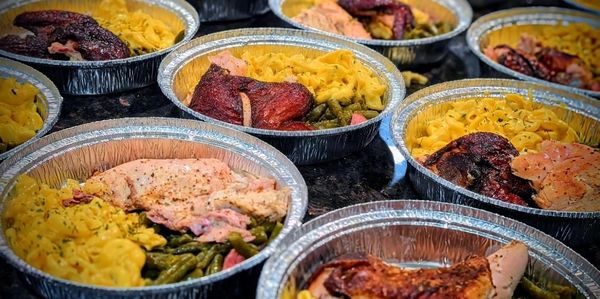 Multiple foil containers filled with macaroni, green beans, and roasted chicken.