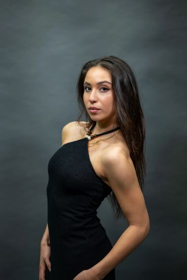 Woman in a black dress posing against a dark background.