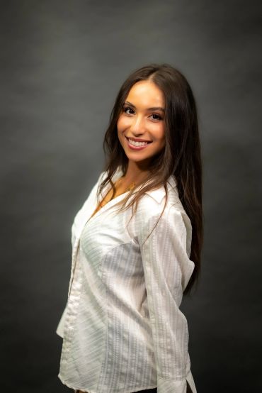 Smiling woman in white shirt against dark background.
