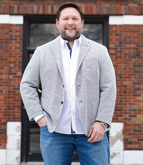Smiling man in casual blazer and jeans posing outdoors.