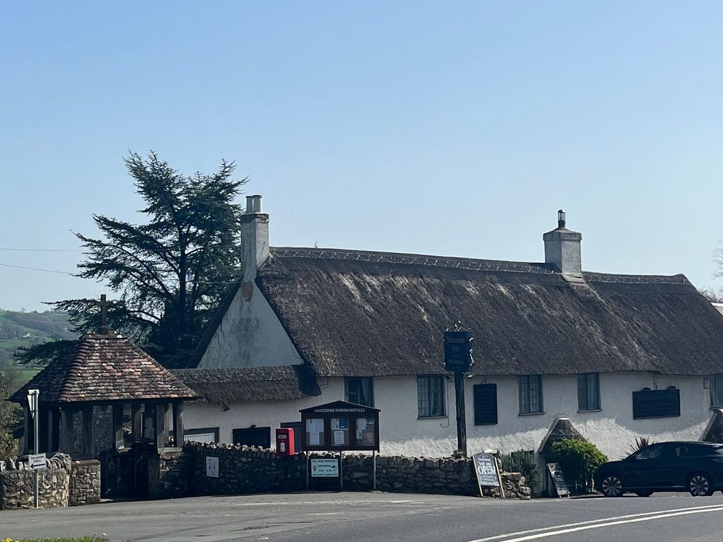 Thatched roof cottage with stone walls and a car parked outside under clear blue sky.