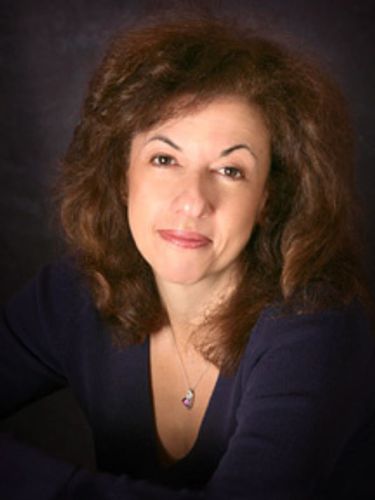 professional headshot of smiling woman with dark brown hair with navy blue necklace