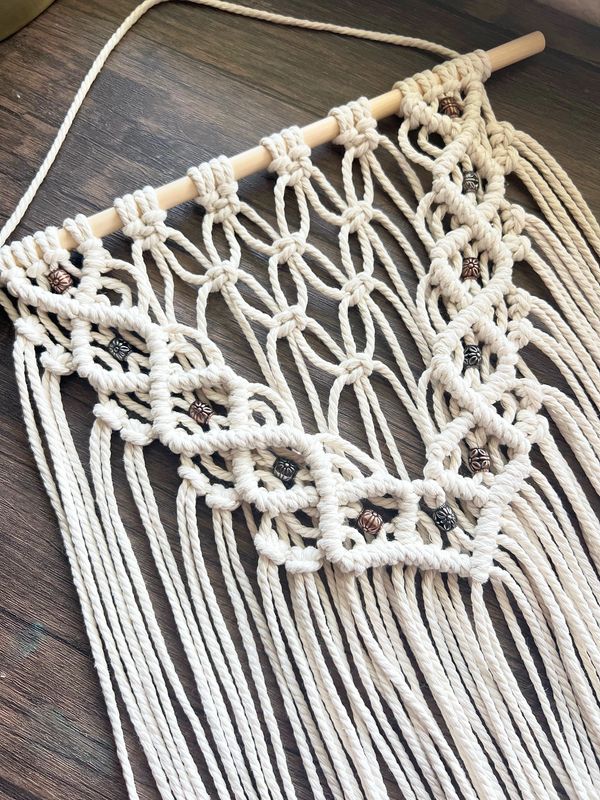 Handcrafted macramé wall hanging with intricate knots and beads on wooden rod.
