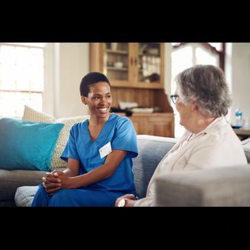 Nurse in blue scrubs smiling and talking with an elderly woman.