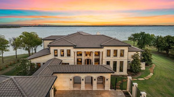 Luxurious lakefront mansion at sunset with a tiled roof and large windows.