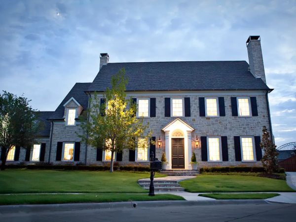 Elegant two-story stone house with bright windows at dusk.