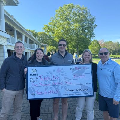 Group of five holds a large $5,000 donation check outdoors.