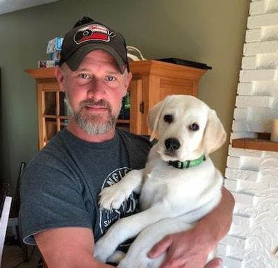 man holding up a white labrador dog